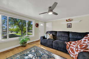 Living room featuring a textured ceiling, wood finished floors, a ceiling fan, and crown molding
