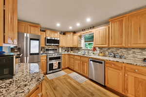Kitchen with light stone countertops, recessed lighting, appliances with stainless steel finishes, light wood-style floors, and decorative backsplash