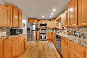 Kitchen featuring light stone counters, backsplash, stainless steel appliances, and recessed lighting
