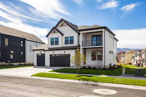 Modern farmhouse style home featuring a balcony, board and batten siding, a front yard, concrete driveway, and an attached garage