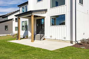 Back of house with board and batten siding, a patio, and a yard