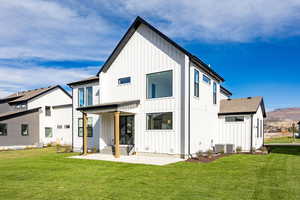 Back of property featuring board and batten siding, a patio area, and a yard