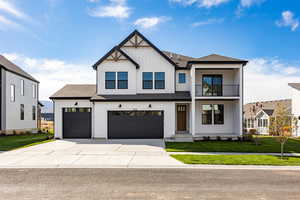 Modern inspired farmhouse featuring board and batten siding, a front yard, a balcony, roof with shingles, and driveway