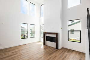 Unfurnished living room with a tiled fireplace, light wood-style flooring, and a towering ceiling