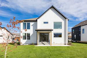 Back of house with board and batten siding, a lawn, a shingled roof, and a patio