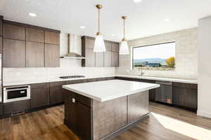 Kitchen featuring tasteful backsplash, stainless steel appliances, a textured ceiling, dark wood-type flooring, and wall chimney exhaust hood