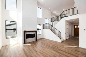 Unfurnished living room featuring a tile fireplace, recessed lighting, light wood-style floors, a high ceiling, and stairway