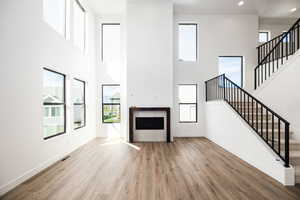 Unfurnished living room with stairway, a fireplace, light wood finished floors, a towering ceiling, and recessed lighting