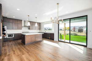 Kitchen with hanging light fixtures, a chandelier, a kitchen island, dark wood-type flooring, and recessed lighting