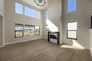 Unfurnished living room featuring a high ceiling, a glass covered fireplace, light wood finished floors, and a chandelier
