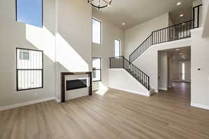 Unfurnished living room with a glass covered fireplace, a high ceiling, light wood-type flooring, recessed lighting, and stairway