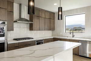 Kitchen featuring wall chimney exhaust hood, appliances with stainless steel finishes, tasteful backsplash, pendant lighting, and modern cabinets