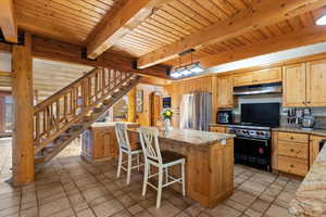 Kitchen featuring freestanding refrigerator, premium stove, a kitchen breakfast bar, a kitchen island, and under cabinet range hood