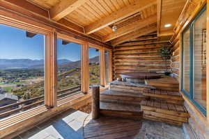 Unfurnished sunroom with log walls, a mountain view, a sauna / steam room, wood ceiling, and stone tile floors