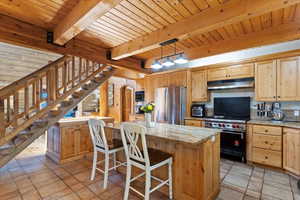 Kitchen featuring stainless steel appliances, arched walkways, light stone countertops, light brown cabinetry, and pendant lighting