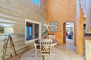 Dining room with arched walkways, a high ceiling, light tile patterned floors, and wood walls
