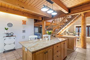 Kitchen with hanging light fixtures, a kitchen island, light stone countertops, a wooden ceiling with exposed beams, and light tile patterned flooring