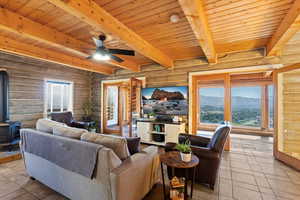 Living area featuring a wood stove, a wood ceiling with exposed beams, rustic walls, and a ceiling fan