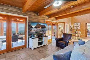 Living room featuring french doors, arched walkways, ceiling fan, a wooden ceiling with exposed beams, and light stone finish floors