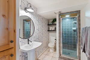 Bathroom with wallpapered walls, light tile patterned flooring, and a stall shower