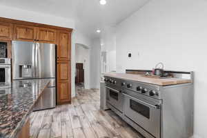 Kitchen with hardwood cabinetry, appliances with stainless steel finishes, recessed lighting, arched walkways, and wood look tile floors