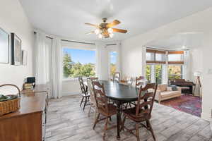 Formal dining room with light wood-style tile flooring, arched walkways, wall of windowsand a ceiling fan