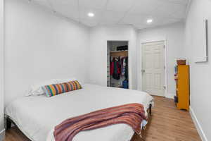 Bedroom with light wood finished floors, a paneled ceiling, recessed lighting, and a closet
