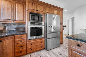 Kitchen featuring hardwood cabinetry, appliances with stainless steel finishes, recessed lighting, backsplash, and wood look tiled floors