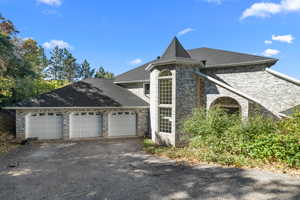 View of front of home with roof with shingles, a 3 car garage, asphalt driveway, and brick siding