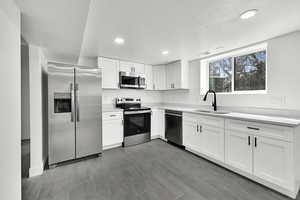 Kitchen featuring stainless steel appliances, white cabinetry, a textured ceiling, recessed lighting, and light stone counters