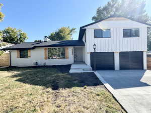 Tri-level home with brick siding, concrete driveway, a chimney, an attached garage, and board and batten siding