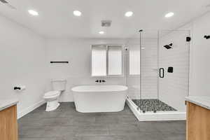 Full bathroom with vanity, a shower stall, a freestanding bath, tile walls, and recessed lighting
