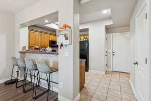 Kitchen featuring a breakfast bar, black appliances, recessed lighting, light tile patterned floors, and brown cabinetry