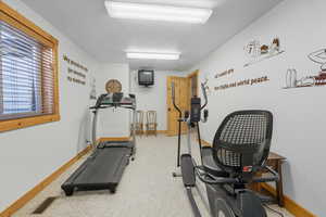 Bedroom currently being used as a workout room with light carpet and a textured ceiling