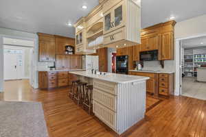 Kitchen with glass insert cabinets, brown cabinets, light wood flooring, a kitchen bar, and open shelves