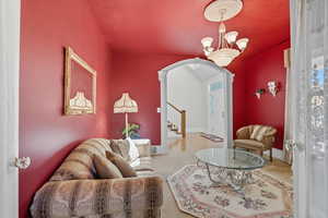 Carpeted living room with arched walkways, stairs, decorative columns, and a chandelier