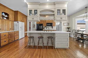 Kitchen featuring light wood finished floors, brown cabinetry, an island with sink, a breakfast bar area, and black appliances