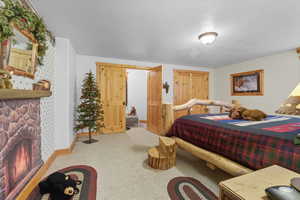 Bedroom with carpet flooring, a stone fireplace, and a textured ceiling