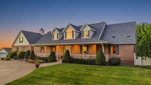 Cape cod-style house featuring brick siding, a porch, a yard, a shingled roof, and a garage