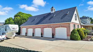 View of side of property featuring a shingled roof, brick, and driveway