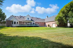 Rear view of house with brick, a deck, a lawn, and roof with shingles