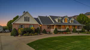 Cape cod home with a front lawn, covered porch, brick siding, curved driveway, and a shingled roof