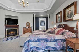 Primary Suite Bedroom with a warm lit fireplace, a raised ceiling, carpet floors, ensuite bathroom, and a chandelier