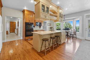 Kitchen featuring black appliances, a kitchen bar, light wood-style floors, an island with sink, and glass insert cabinets