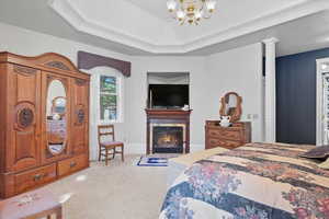Primary Suite bedroom with a gas fireplace, a chandelier, and a tray ceiling