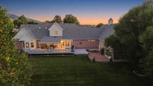Back of property at dusk featuring a yard, a deck, and roof with shingles
