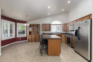 Kitchen featuring appliances with stainless steel finishes, a kitchen island, a kitchen bar, open shelves, and dark countertops