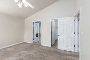 Unfurnished bedroom featuring light carpet, a walk in closet, a ceiling fan, and high vaulted ceiling