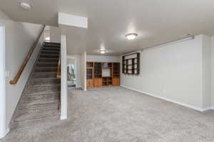 Basement featuring a textured ceiling, light carpet, and stairs