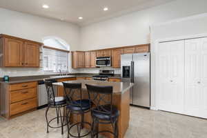 Kitchen with a breakfast bar area, stainless steel appliances, a center island, dark countertops, and a high ceiling